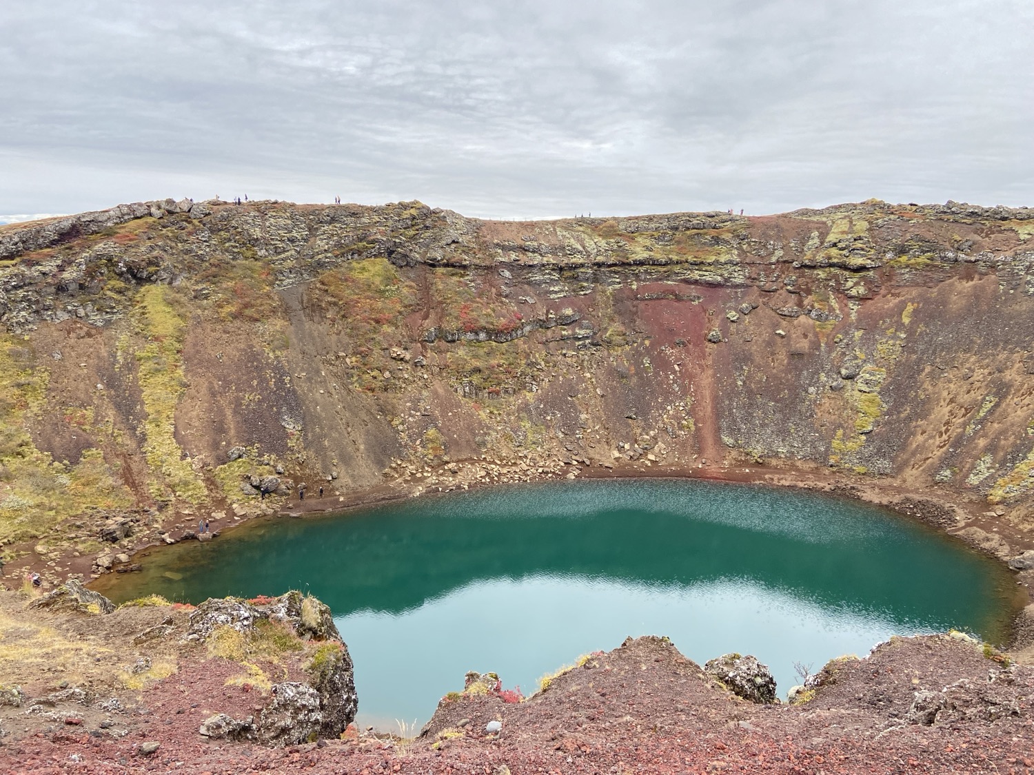 A teal lake in the bottom of a red volcanic crater