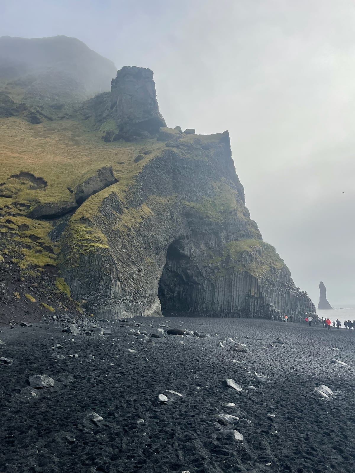 White surf running up the black sand at Reynisfjara, the sea stacks beyond