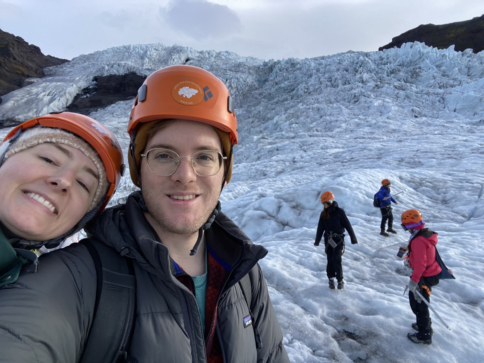 Two hikers in helmets on the glacier, a guided group crossing the ice behind