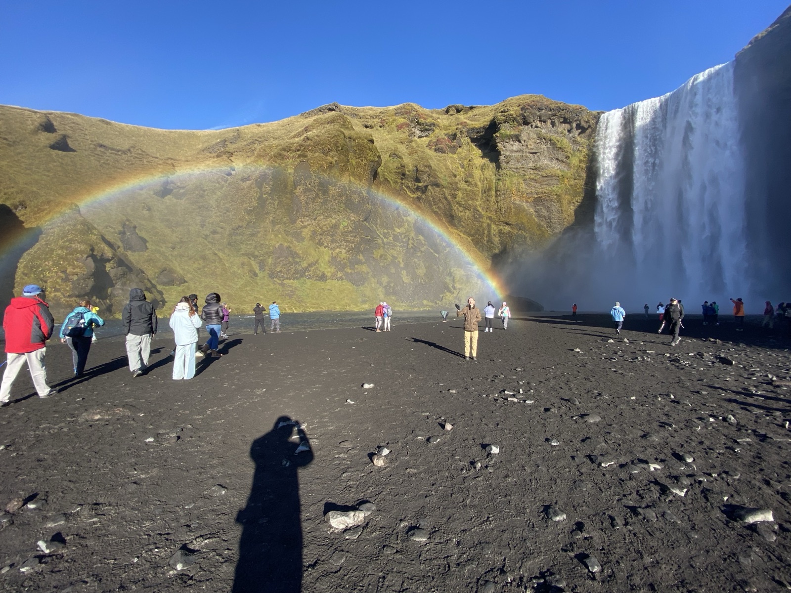 People standing in a rainbow at the foot of Skogafoss