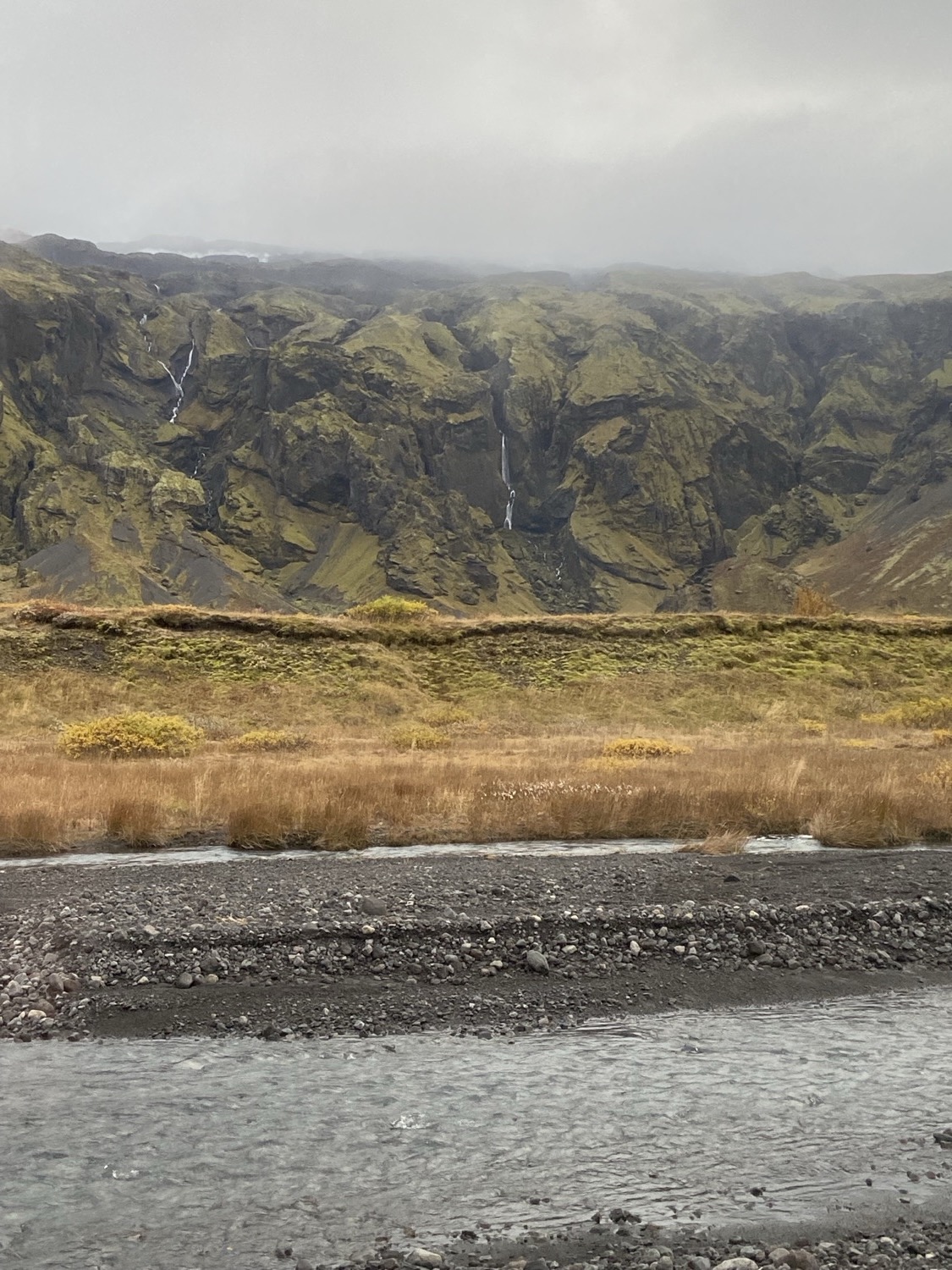 Thin waterfalls down mossy mountains above a black-sand river