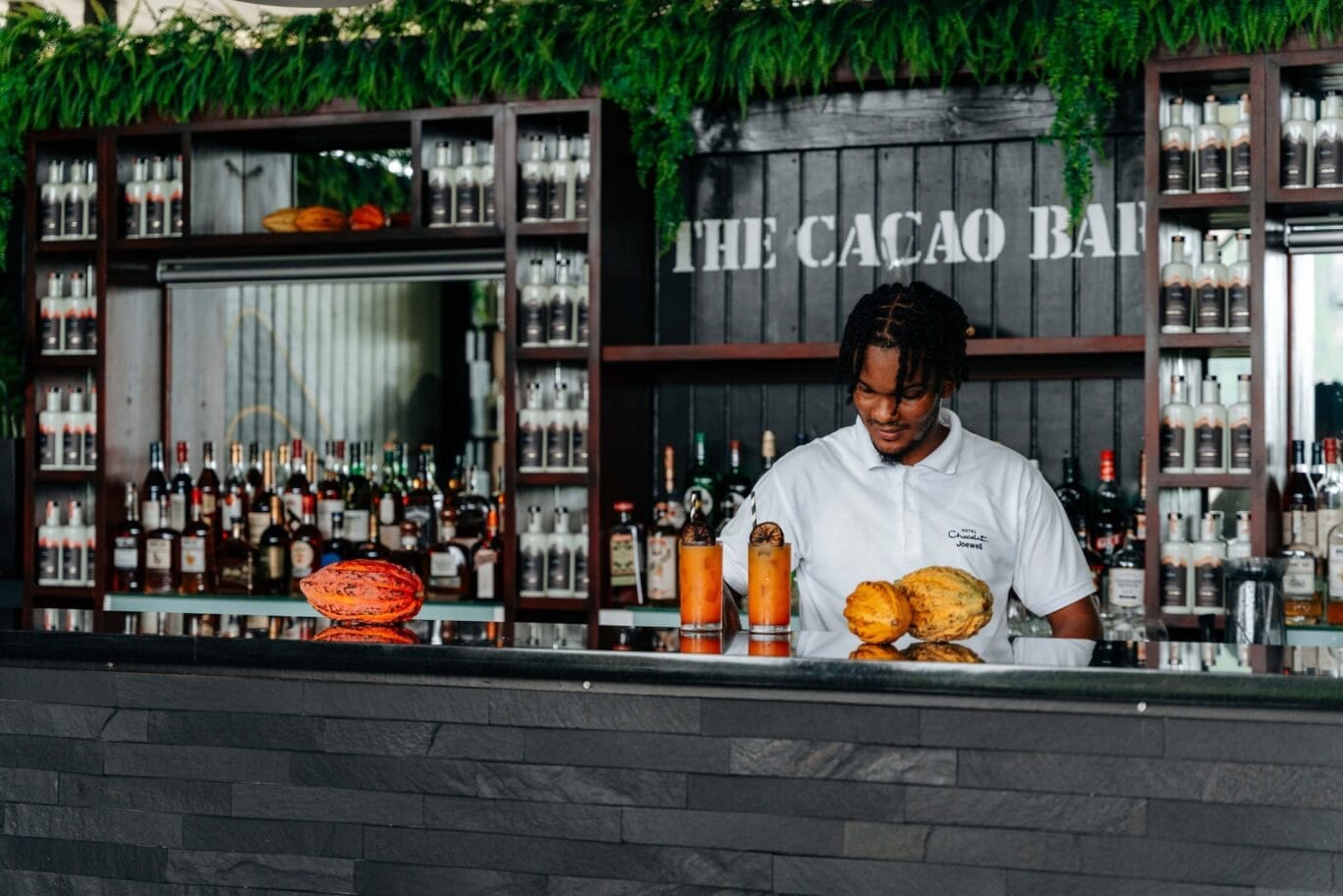 A bartender at The Cacao Bar mixing cacao cocktails below shelves of rum, cacao pods on the counter