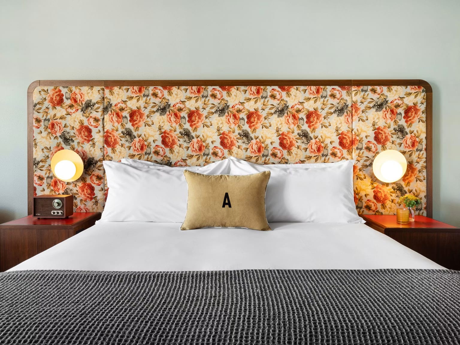 A guest room at ARRIVE Albuquerque with a floral upholstered headboard, globe lamps and a vintage radio