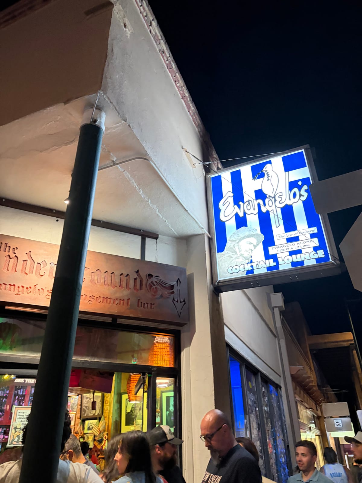 The lit blue-and-white Evangelo's cocktail lounge sign at night with a crowd outside