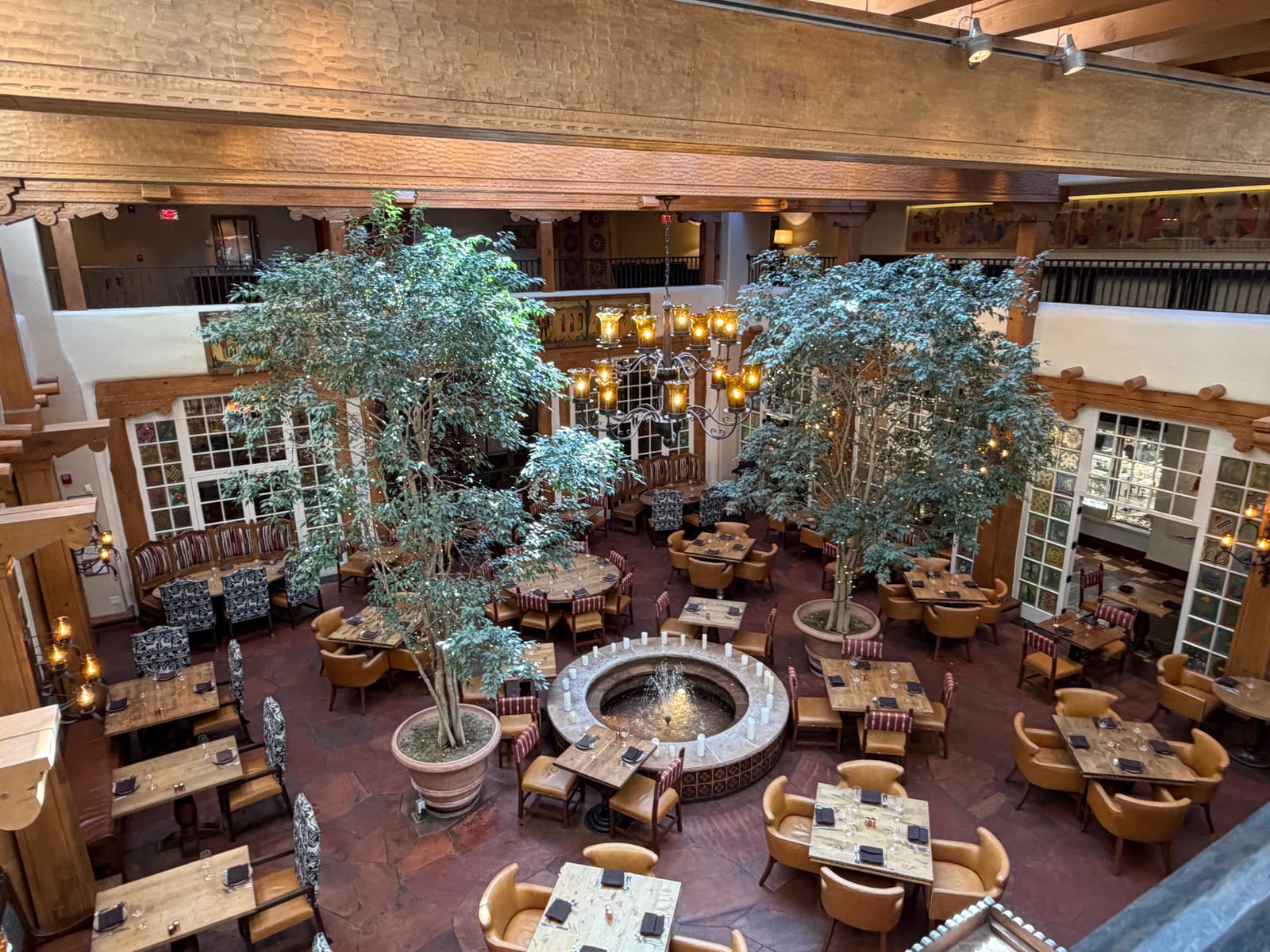 The skylit atrium restaurant at La Fonda on the Plaza, with trees, a stone fountain and carved wooden beams