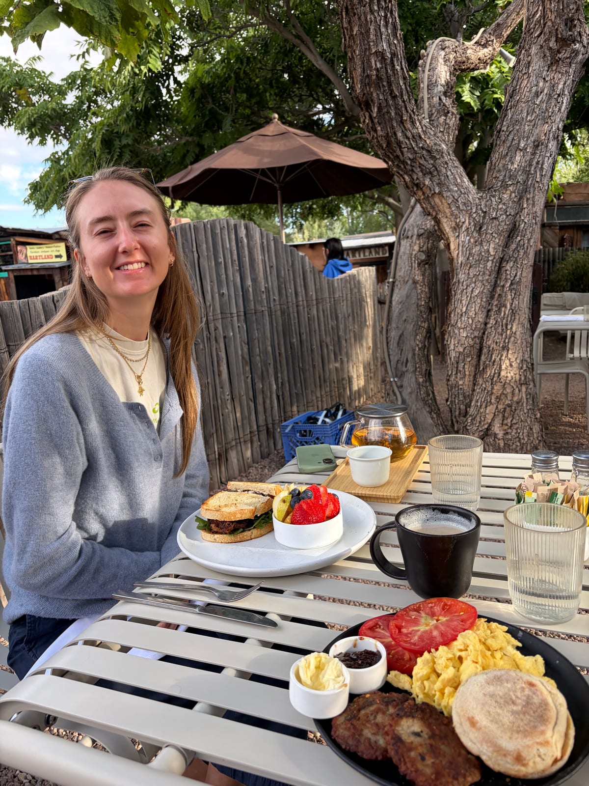 Breakfast plates and a glass teapot on a courtyard table under a cottonwood