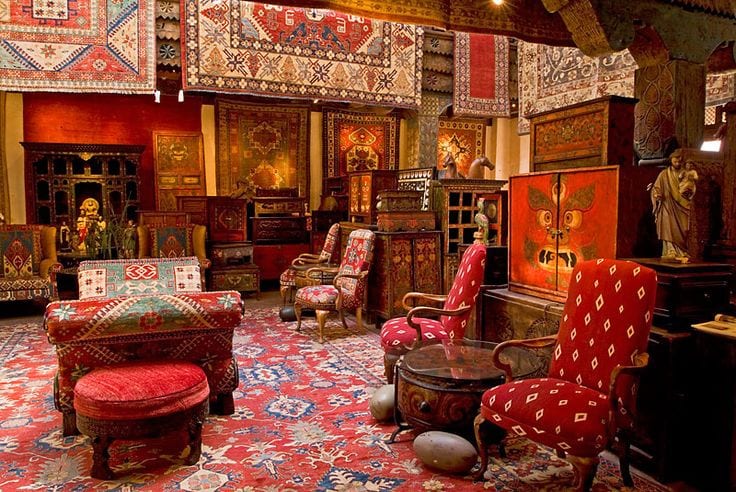 A showroom at Seret and Sons hung with Persian rugs above carved and painted antique furniture