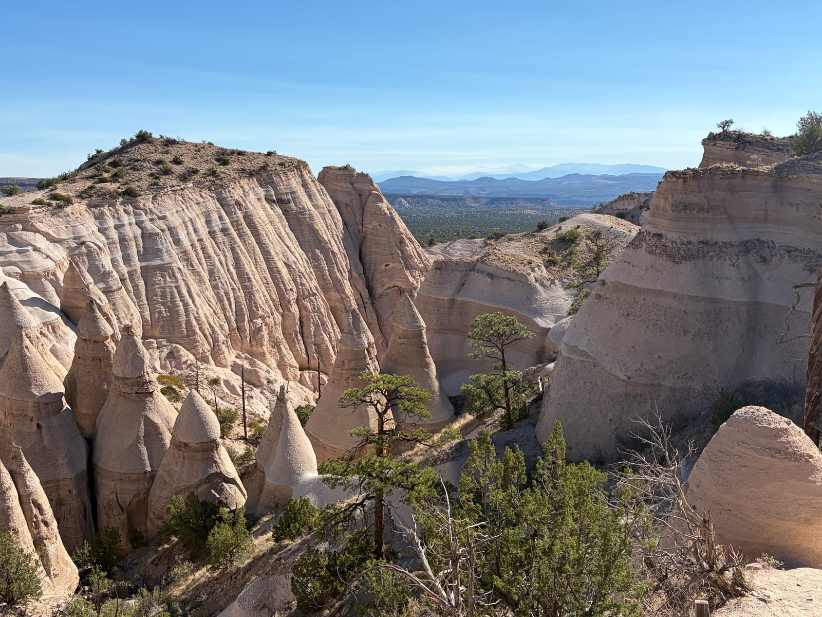 A wide view from the mesa top over the hoodoo field at Tent Rocks to distant mountains