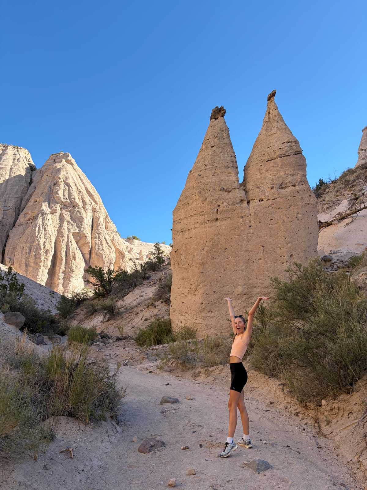 A hiker with arms raised beneath the tent-shaped hoodoos at Kasha-Katuwe