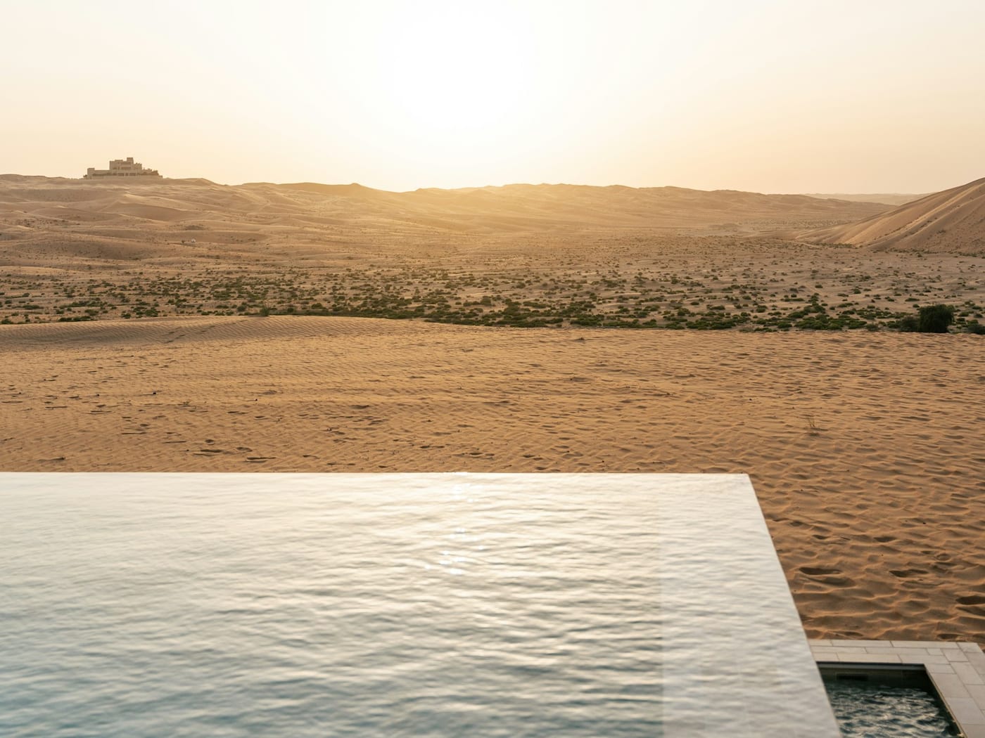 An infinity pool at the edge of desert dunes at sunset